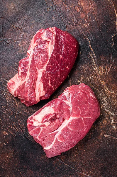 Raw Chuck eye roll beef steak on butcher table. Dark background. Top view