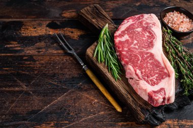 Çiğ New York bifteği ya da tahta bir tahtanın üzerinde striploin. Koyu ahşap arka plan. Üst Manzara. Boşluğu kopyala