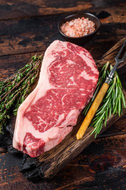 Çiğ New York bifteği ya da tahta bir tahtanın üzerinde striploin. Koyu ahşap arka plan. Üst görünüm