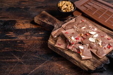 Fındıklı, fıstıklı, kızılcıklı ve dondurulmuş ahududulu ev yapımı sütlü çikolata. Koyu ahşap arka plan. Üst Manzara. Boşluğu kopyala