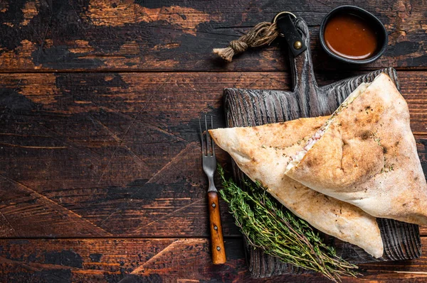 Hemlagad Calzone stängd pizza med skinka och ost på träskiva. Mörk trä bakgrund. Högst upp. Kopiera utrymme — Stockfoto