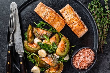 Kızarmış somon fileto biftekli ve roka salatalı balık yemeği. Siyah arka plan. Üst görünüm