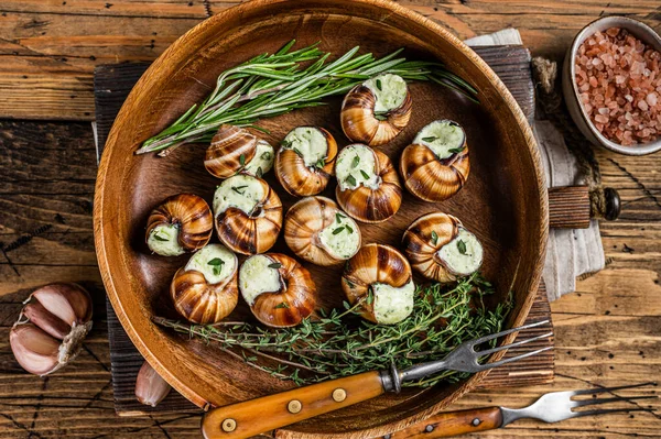 Γαλλικά σαλιγκάρια Escargot με βούτυρο σκόρδου σε ξύλινο πιάτο. Ξύλινο φόντο. Άνω όψη — Φωτογραφία Αρχείου