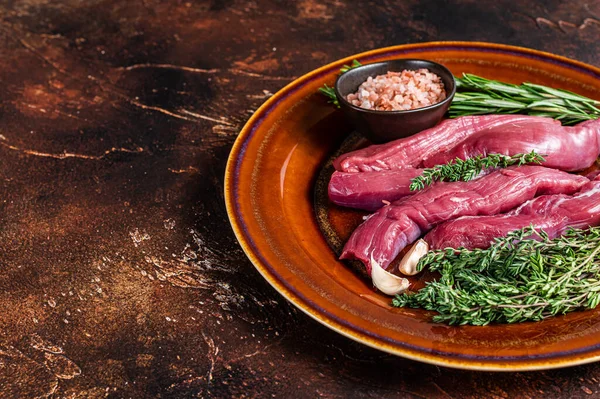 Uncooked Raw lamb tenderloin Fillet Meat in rustic plate with thyme and rosemary. Dark background. Top view. Copy space — Stock Photo, Image