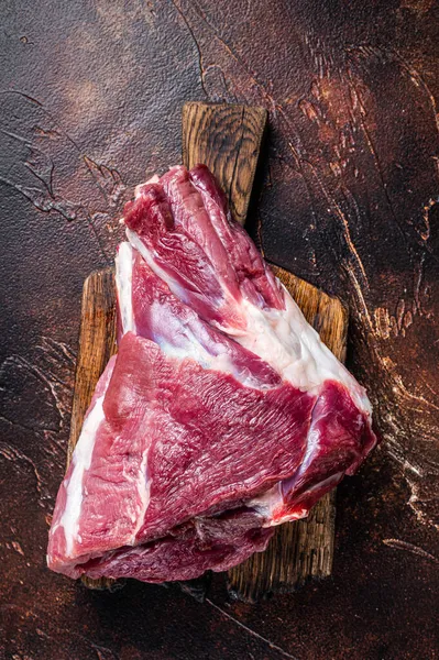 生羊肉羊肉大腿放在肉桌上.黑暗的背景顶部视图 — 图库照片