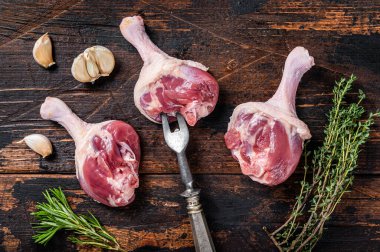 Et çatalında taze çiğ ördek bacağı ve otlar. Koyu ahşap arka plan. Üst görünüm