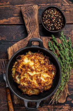 Kızarmış patates gözlemesi ya da tavada otlu börek. Koyu ahşap arka plan. Üst görünüm