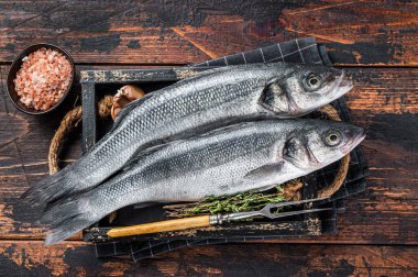Tahta tepside otlu deniz levreği ya da çiğ balık. Koyu ahşap arka plan. Üst görünüm