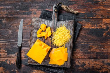 Tahta bir tahtanın üzerinde rendelenmiş ve oyulmuş Cheddar Cheese. Koyu ahşap arka plan. Üst görünüm