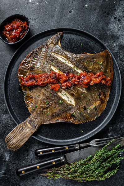 Roasted Flatfish or Flounder in a tomato sauce. Black background. Top view