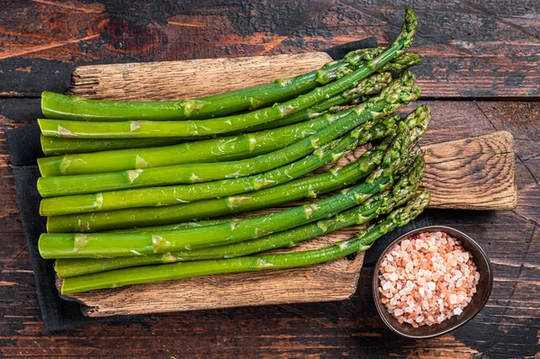 Fresh green asparagus on a wooden cutting board. Dark wooden background. Top view — Stock Photo, Image