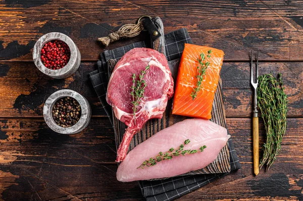 Bifes crus - salmão de peixe, carne de vaca e filé de peito de peru em uma tábua de redução. Fundo de madeira. Vista superior — Fotografia de Stock