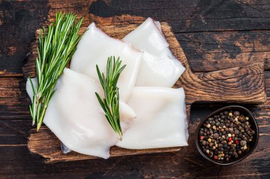 Ahşap bir tahtada biberiyeli çiğ kalamar ya da mürekkep balığı. Koyu ahşap arka plan. Üst görünüm