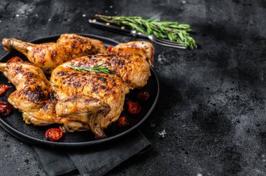 Tütün tavuğu tabakta otlar ve domatesle. Siyah arka plan. Üst Manzara. Boşluğu kopyala