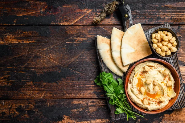 Hummus paste with pita bread, chickpea and parsley in a wooden bowl. Dark wooden background. Top view. Copy space — Stock Photo, Image