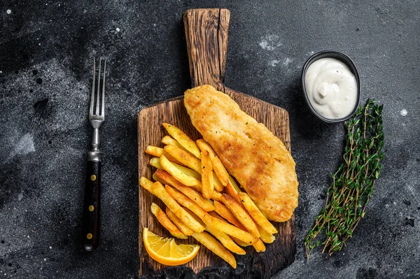Fisk och chips maträtt med pommes frites på träskiva. Svart bakgrund. Ovanifrån — Stockfoto