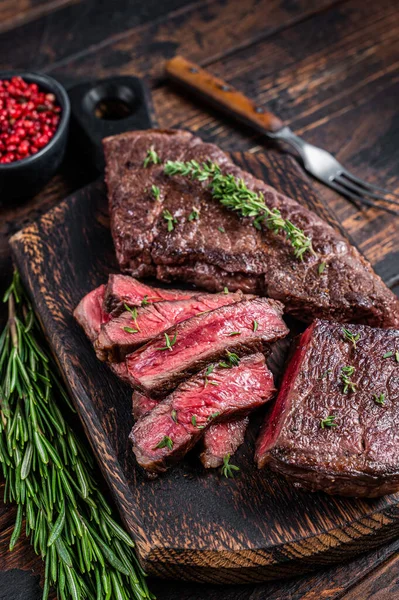 Bife de carne de vaca de saia fatiada grelhada em uma placa de corte com ervas. Fundo de madeira escuro. Vista superior — Fotografia de Stock