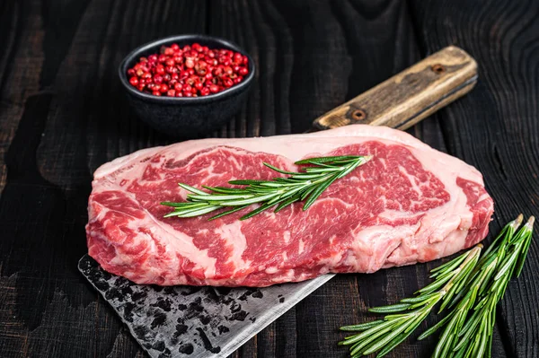 Kasap satırının üzerinde taze çiğ biftek var. Siyah ahşap arka plan. Üst görünüm