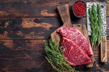 Çiğ Denver et satırıyla kasap tahtasında siyah angus bifteği kesti. Koyu ahşap arka plan. Üst Manzara. Boşluğu kopyala