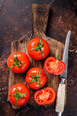 Tahta kesme tahtasıyla kırmızı kiraz domateslerini kes. Karanlık arka plan. Üst görünüm