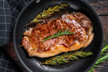 Tavada ızgara çizgili biftek ve otlar. Koyu ahşap arka plan. Üst görünüm