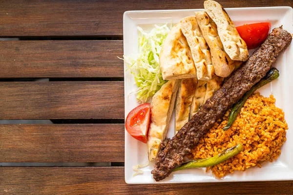 Kebab d'Adana turque dans une assiette avec poivrons marinés, pain et riz pilaf. Vue de dessus. Espace de copie — Photo