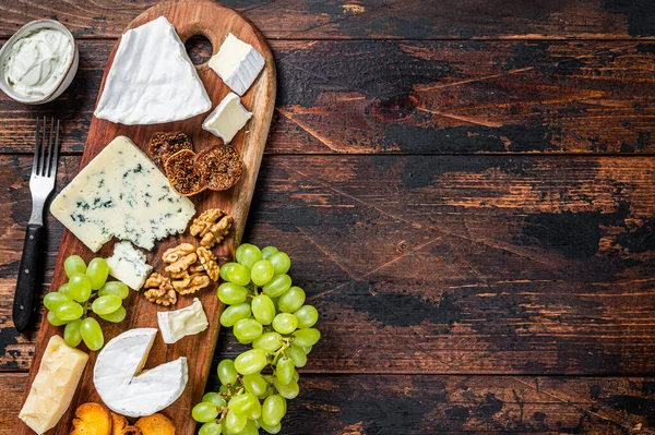 Placa de queijo variada com Brie, Camembert, Roquefort, parmesão, queijo creme azul, uva e nozes. Fundo de madeira escuro. Vista superior. Espaço de cópia — Fotografia de Stock