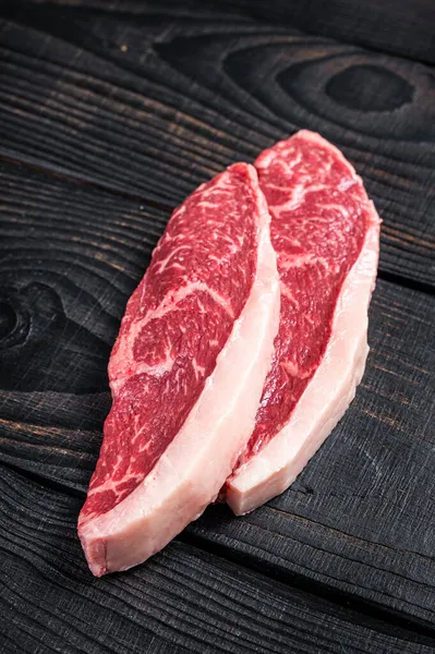 生のランプステーキや肉屋のテーブルの上のサーロインキャップ牛肉ステーキ。黒い木製の背景。トップ表示 — ストック写真