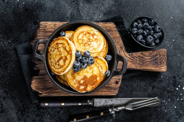 Pancake dengan blueberry segar dan sirup maple dalam panci. Latar belakang hitam Tampilan Atas — Stok Foto