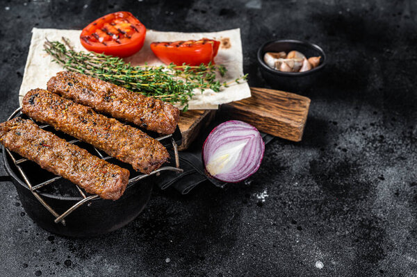 BBQ adana shish kebab on a grill with bread and tomato. Black background. top view. Copy space