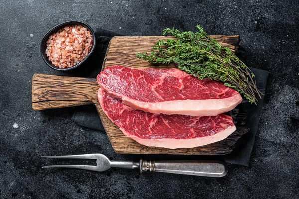 未煮熟的生肉排骨牛排或顶部牛腰肉帽牛肉牛排在木板上。黑色背景。顶部视图 — 图库照片