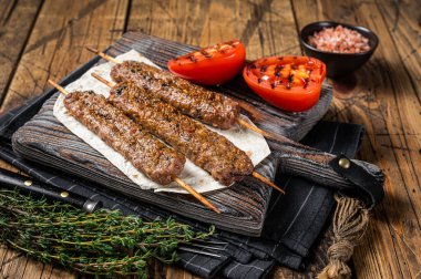 Kızarmış Türk Adana şiş kebabı ızgara domatesle birlikte tahtada. Ahşap arka plan. en üstteki görünüm