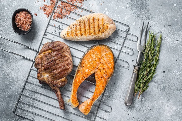 Ensemble de steaks grillés au barbecue saumon, bœuf et dinde sur un gril. Fond gris. Vue du dessus — Photo