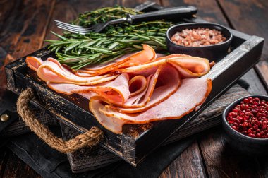 Italian Prosciutto cotto Ham slices in wooden tray with thyme and rosemary. Wooden background. Top view clipart