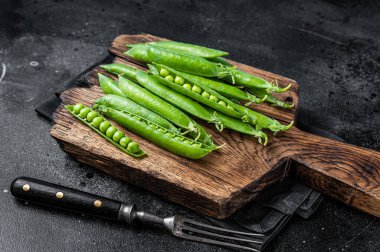 Taze bezelyeler ve yeşil bezelye kabukları ahşap bir kesme tahtasında. Siyah arka plan. Üst görünüm