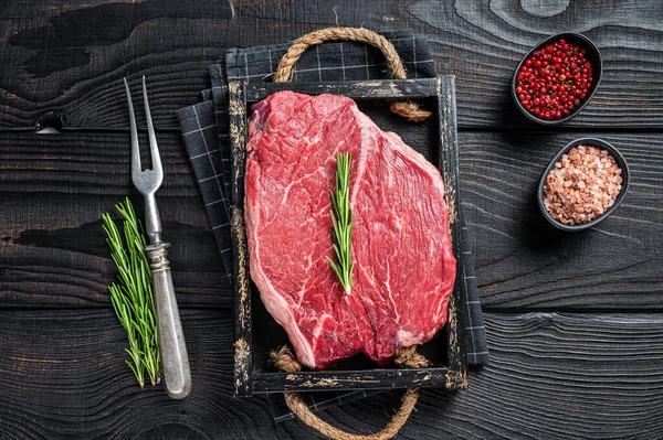 Hovězí syrové filety na steaky v dřevěném podnosu s bylinkami. Černé dřevěné pozadí. Horní pohled — Stock fotografie