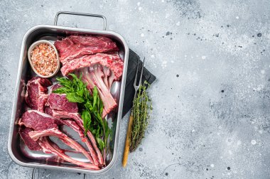 Pişmemiş çiğ kuzu eti, çelik mutfak tepsisinde koyun pirzolası. Gri arka plan. Üst Manzara. Boşluğu kopyala
