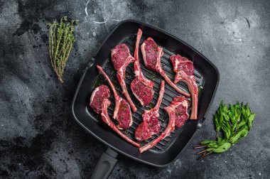 Çiğ kuzu eti, tavada kuzu pirzolası ve otlar pişmeye hazır. Siyah arka plan. Üst görünüm