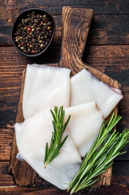 Ahşap bir tahtada biberiyeli çiğ kalamar ya da mürekkep balığı. Koyu ahşap arka plan. Üst görünüm