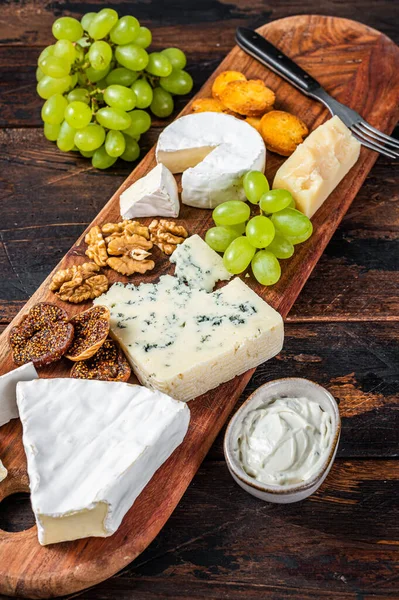 Placa de queijo variada com Brie, Camembert, Roquefort, parmesão, queijo creme azul, uva e nozes. Fundo de madeira escuro. Vista superior — Fotografia de Stock