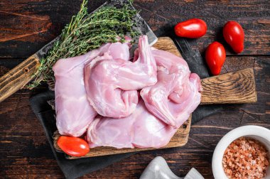 Kekikle kasap tahtasında çiğ tavşan bacağı. Koyu ahşap arka plan. Üst görünüm