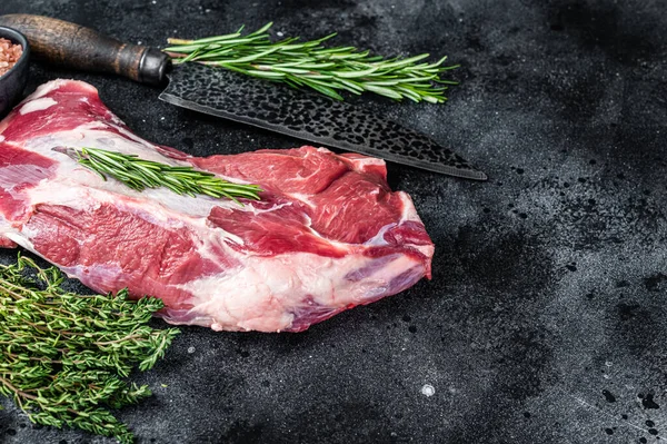Fresh Raw lamb or goat shoulder meat with butcher knife. Black background. Top view. Copy space