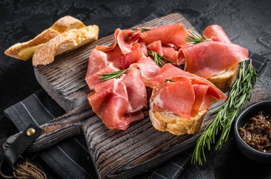 Domatesli tost ve jambonlu jambon dilimleri, ahşap tahtada jambonlu jambonlu jambonlu jambon. Siyah arka plan. Üst görünüm