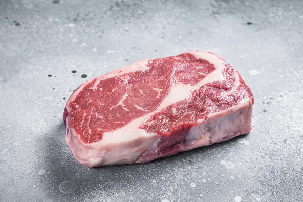 生のリブアイステーキ、肉屋の板の上の牛肉の霜降り肉。灰色の背景。トップ表示 — ストック写真