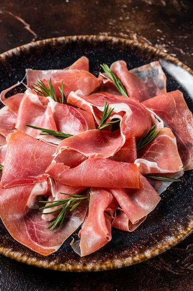 Trozos de prosciutto crudo parma o jamón serrano con romero. Fondo oscuro. Vista superior —  Fotos de Stock