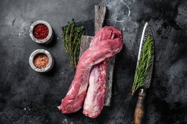 Sığır filetosu çiğ et, ahşap tahtada pişirilmemiş fileto ve bitkiler. Siyah arka plan. Üst görünüm