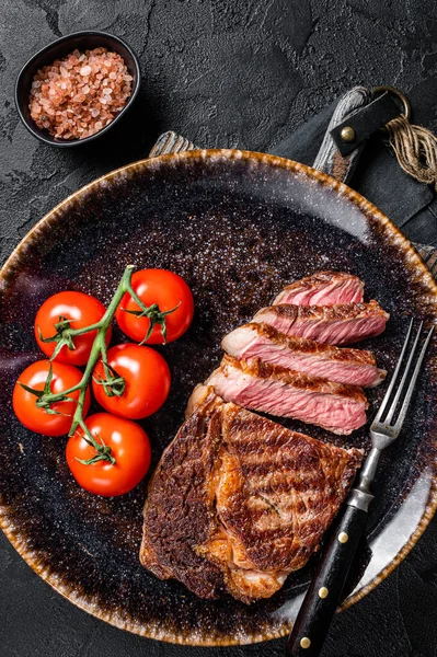 Gegrilde rib oogsteak, ribeye rundvlees gemarmerd vlees op een bord met tomaat. Zwarte achtergrond. bovenaanzicht — Stockfoto