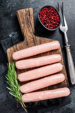 Biberiyeli ahşap bir tahtanın üzerinde taze çiğ tavuk ve hindi eti sosisi. Siyah arka plan. Üst görünüm
