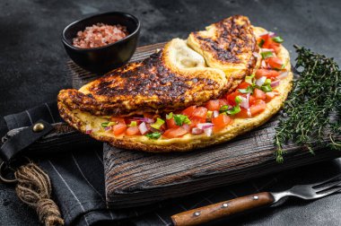 Doldurulmuş domatesli omlet, kırmızı dolma biber ve ahşap tahtada soğan. Siyah arka plan. Üst görünüm