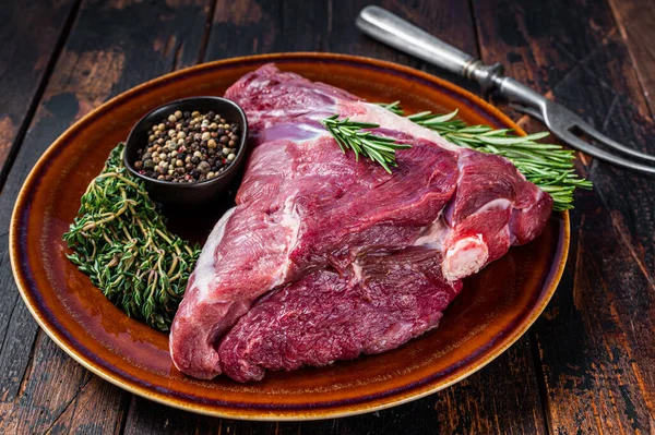 Çiğ kuzu budu ya da bacağı biberiyeli ve kekik otlu. Koyu ahşap arka plan. Üst görünüm